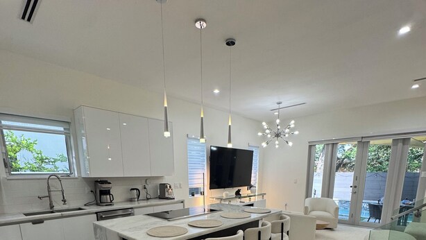 Una cocina moderna con una isla central, taburetes de bar, un televisor de pantalla plana grande y un comedor con mesa y sillas de vidrio.