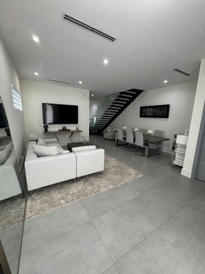 A modern living room with a grey sofa, a flat-screen TV, and a staircase leading to an upper level. - 3-bedroom Luxury Townhouse w Private Pool and Parking (Miami)