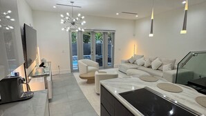 Una cocina moderna con una isla grande, un comedor con mesa de vidrio y una sala de estar con sofá y sillones.