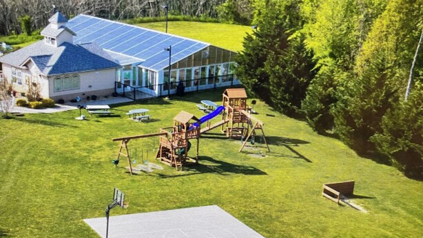 A playground with swings and slides, a picnic table, and a building with a solar panel roof.