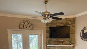 A living room with a stone fireplace, leather sofas, a coffee table, and a ceiling fan.