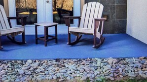 A porch with two Adirondack chairs and a small table, a door, and a wall with a textured pattern.