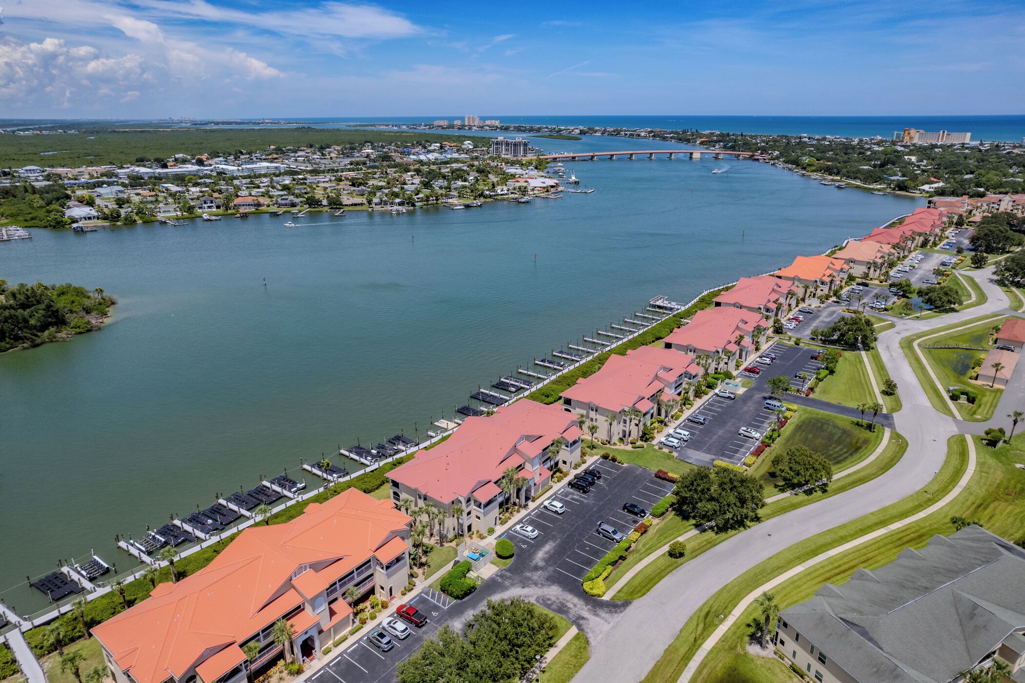 An aerial view of a coastal town with a marina, red-roofed buildings, and a bridge in the background.