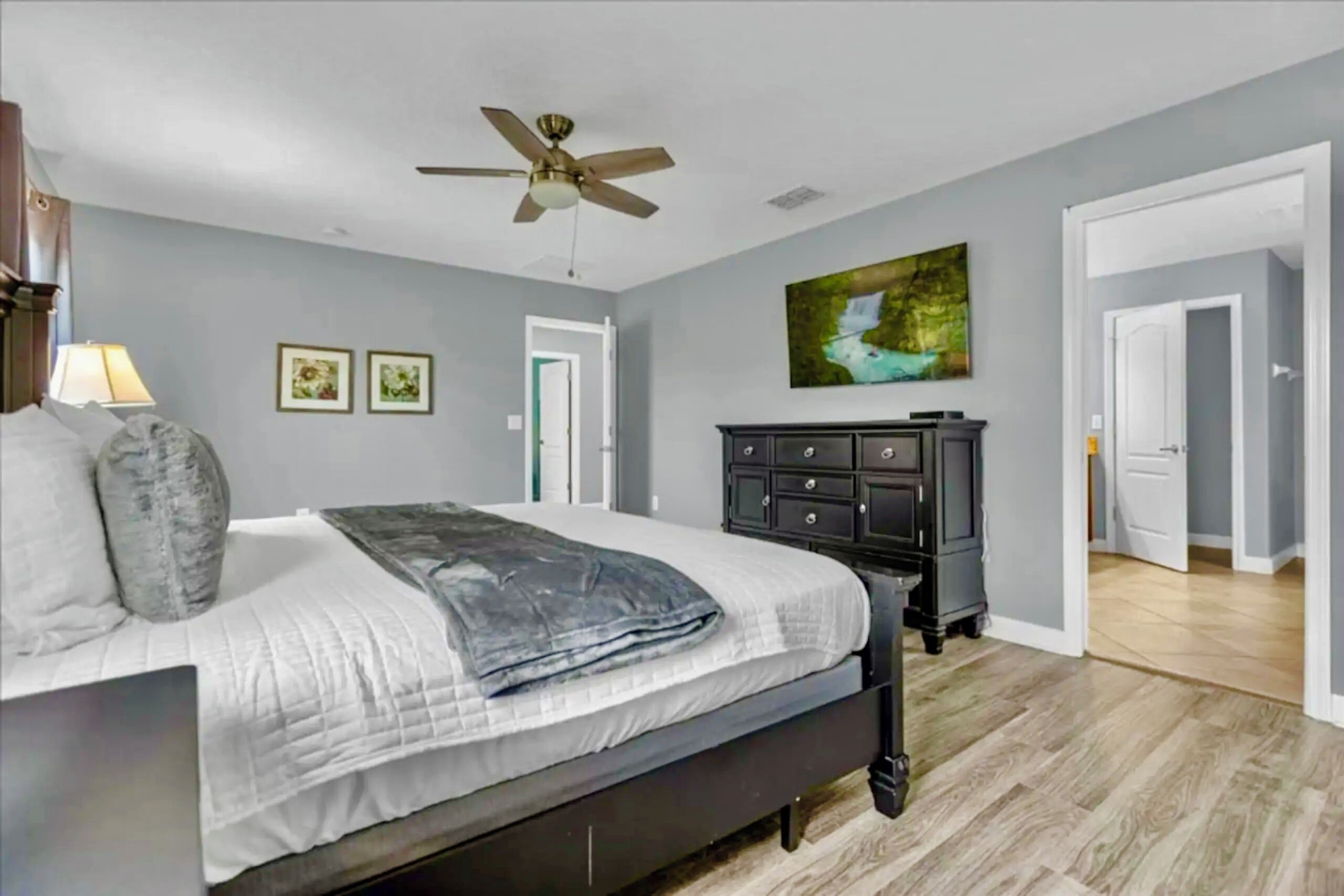 Une chambre à coucher avec un lit, un ventilateur de plafond, une commode et un tableau au mur.