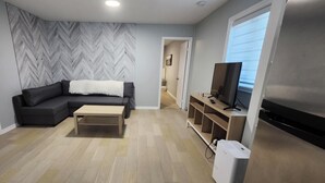A modern living room with a sectional sofa, a coffee table, a TV on a wooden stand, and a herringbone-patterned wall. - Welcome to Mymy! (Sept-Îles)