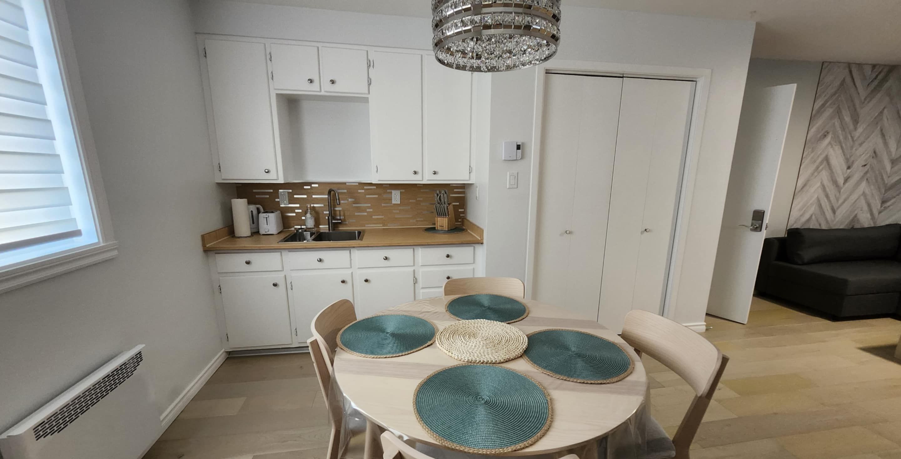 Une cuisine moderne avec des armoires blanches, un comptoir en bois et un lustre. On y trouve une table à manger avec des chaises et des sets de table.