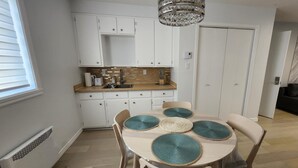 Una cocina moderna con armarios blancos, encimera de madera y una araña. Hay una mesa de comedor con sillas y manteles individuales.