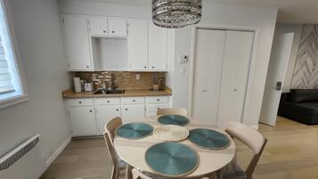 Une cuisine moderne avec des armoires blanches, un comptoir en bois et un lustre. On y trouve une table à manger avec des chaises et des sets de table.