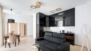 Een moderne woonkamer met een zwarte bank, een glazen salontafel en een eethoek met een houten tafel en stoelen.