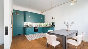 A modern kitchen with teal cabinets, a wooden herringbone floor, and a dining area with a dark table and white chairs. - Mokotowska Superior Apartment (Warszawa)