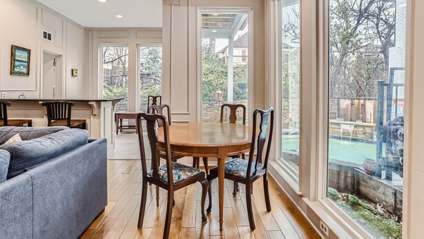 A dining area with a round table, chairs, and a view of the backyard through large windows.
