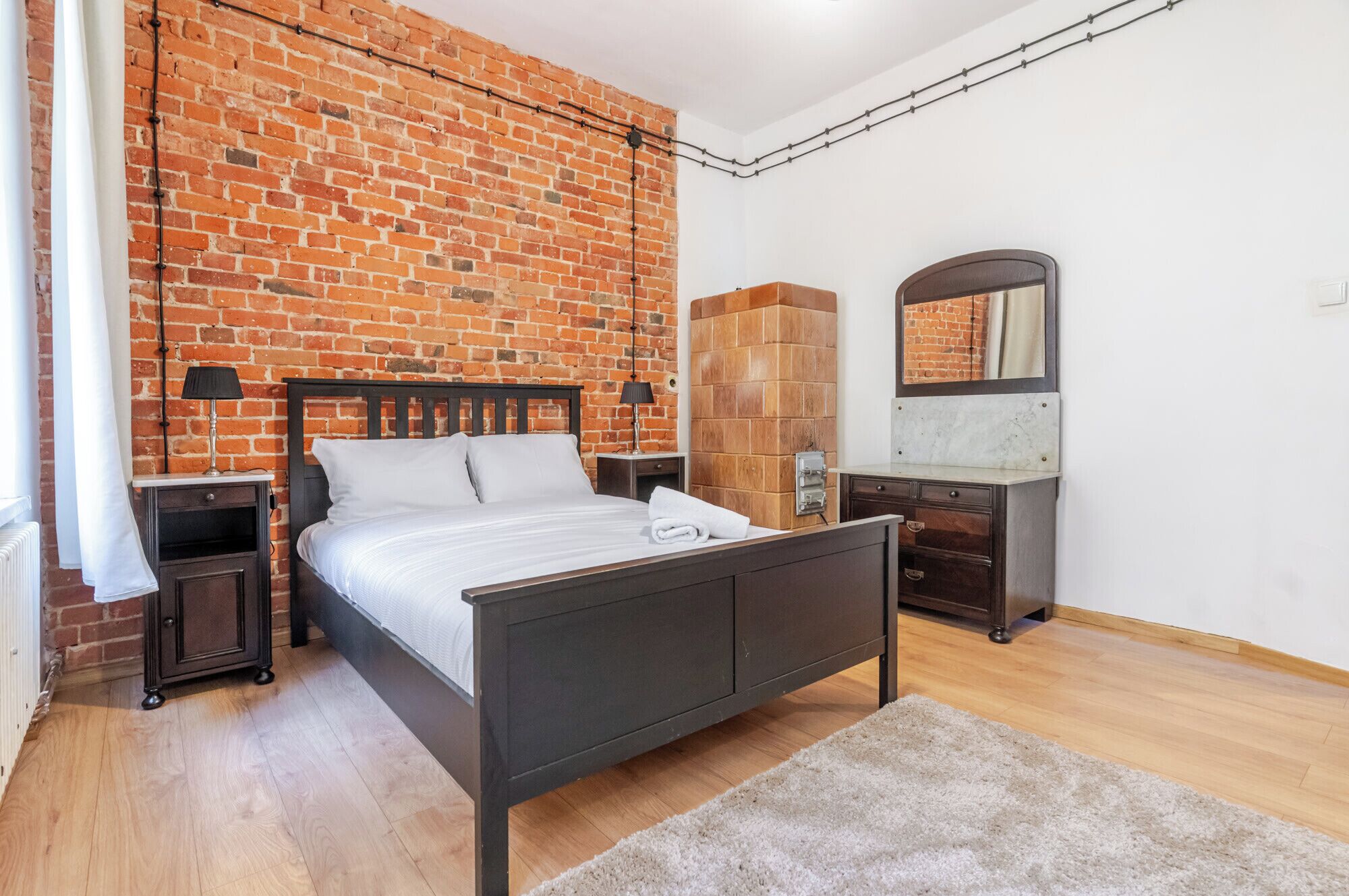 A bedroom with a brick wall, a bed, a dresser, a mirror, and a nightstand.