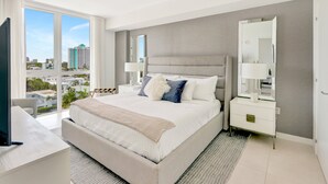 A modern hotel room with a large bed, a TV, a desk, and a view of the city. - FTL Tiffany Topaz: 7th FL, Rooftop Pool, Gym, Walk to Beach (Fort Lauderdale)
