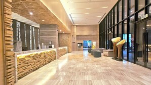 Een moderne receptie met een houten balie, een zithoek met banken en een grote glazen wand.