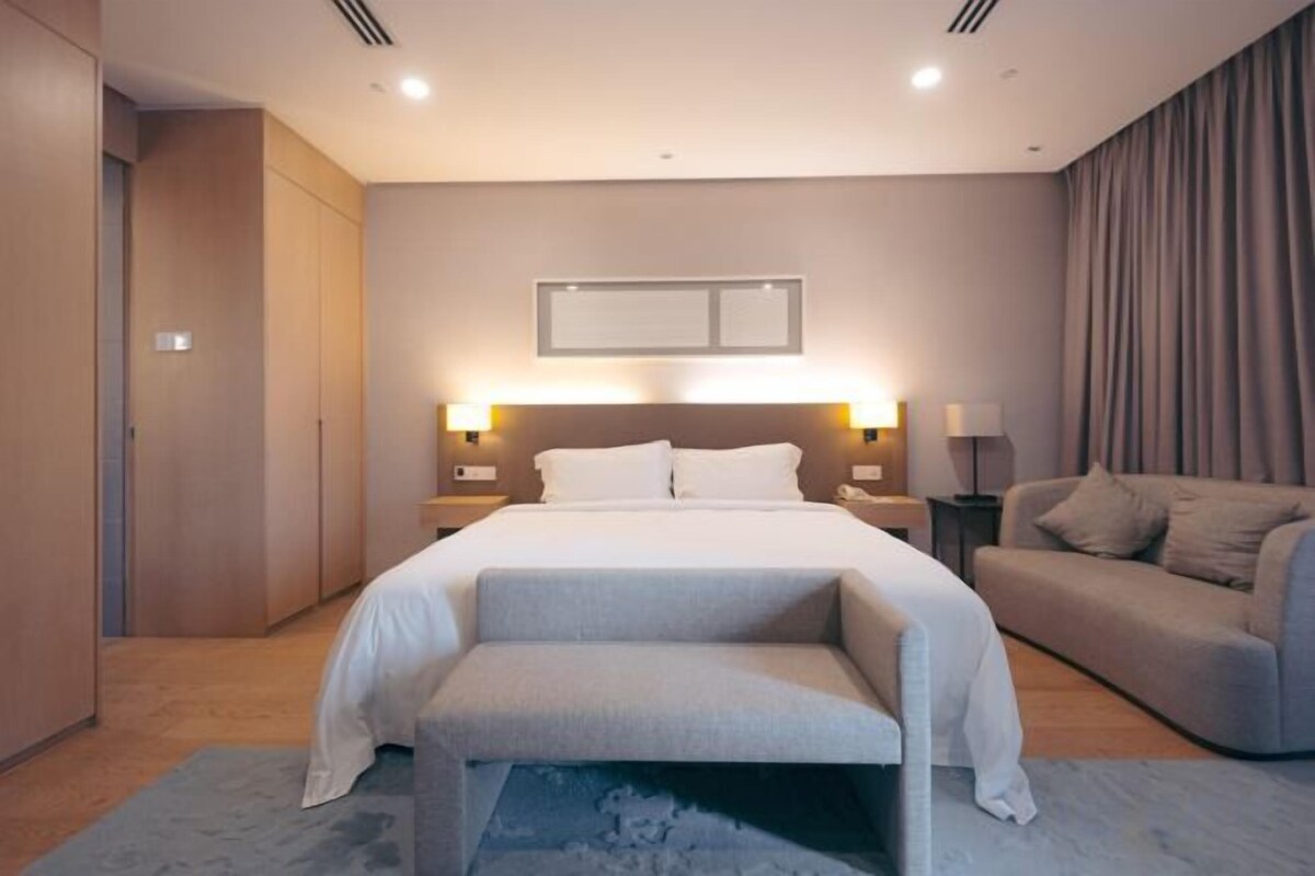 A modern hotel room with a large bed, bedside tables, a sofa, and a bench.
