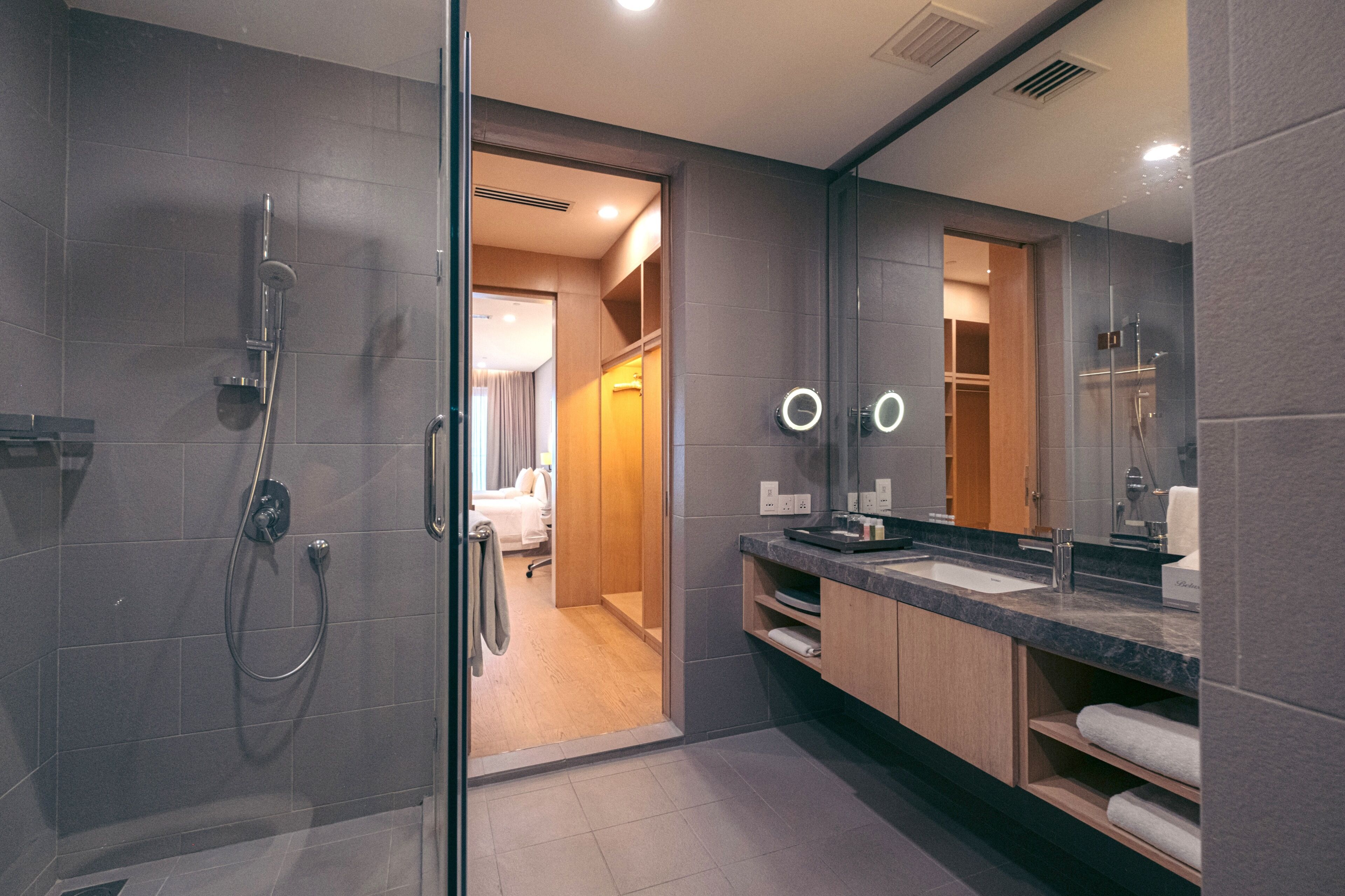 A modern bathroom with a glass shower enclosure, a vanity with a dark countertop, and a large mirror.
