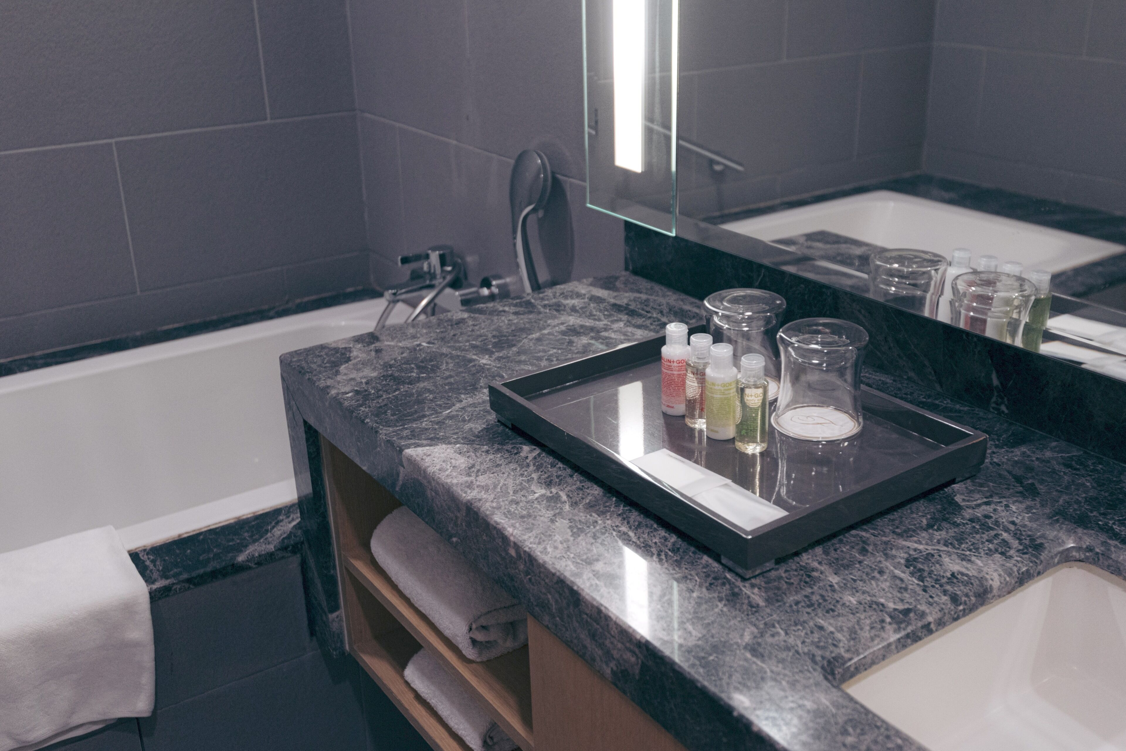 A bathroom with a marble countertop, a sink, a mirror, and toiletries.