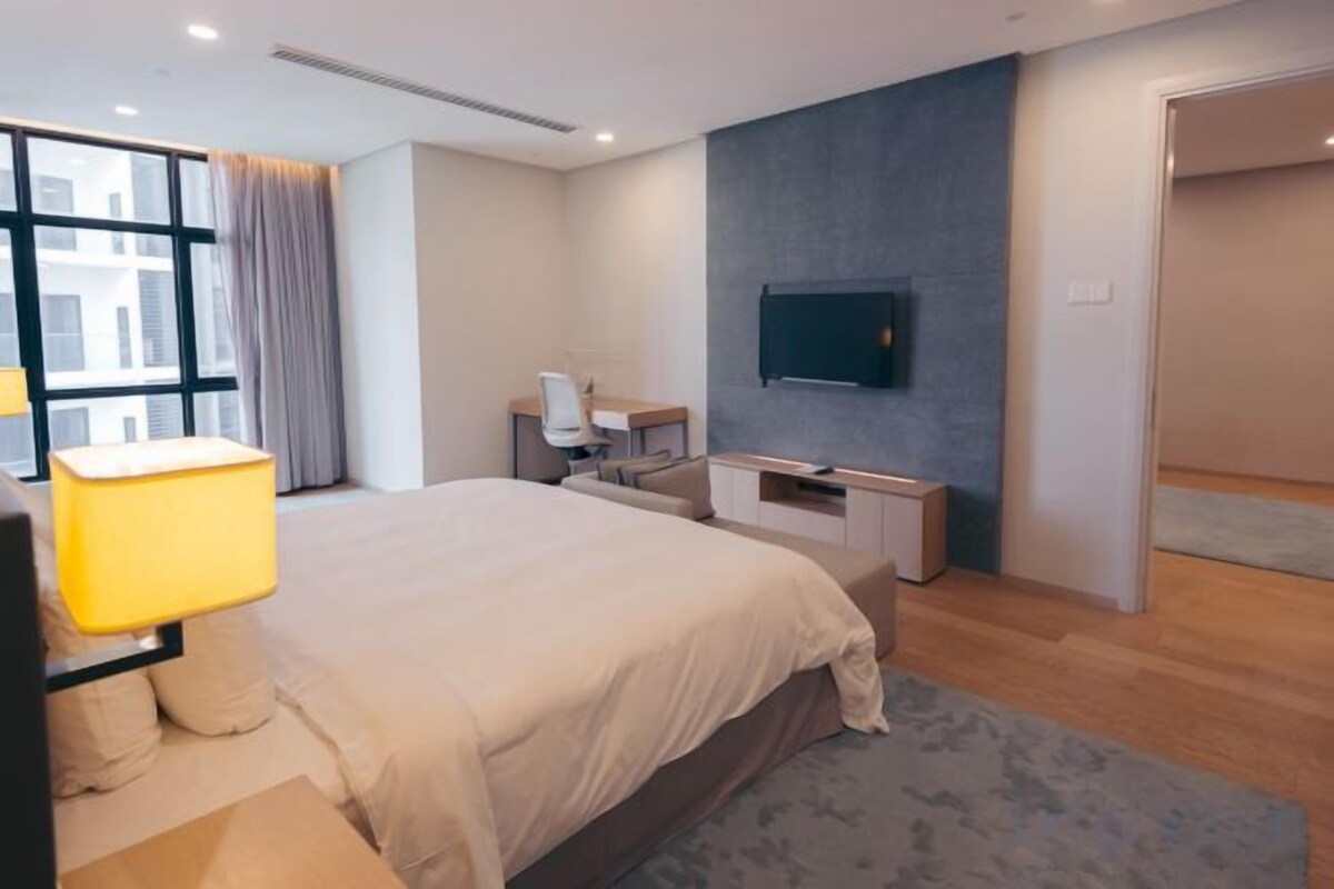 A modern hotel room with a large bed, a desk, a TV, and a window with curtains.