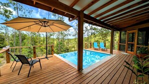 Une terrasse en bois avec une piscine, des chaises d’extérieur et un grand parasol.