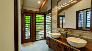 Une salle de bain moderne avec deux grands lavabos, un grand miroir et une vue sur la verdure à travers les portes en verre.