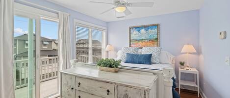A bedroom with a bed, a dresser, a ceiling fan, a window with blinds, and a view of the outside.
