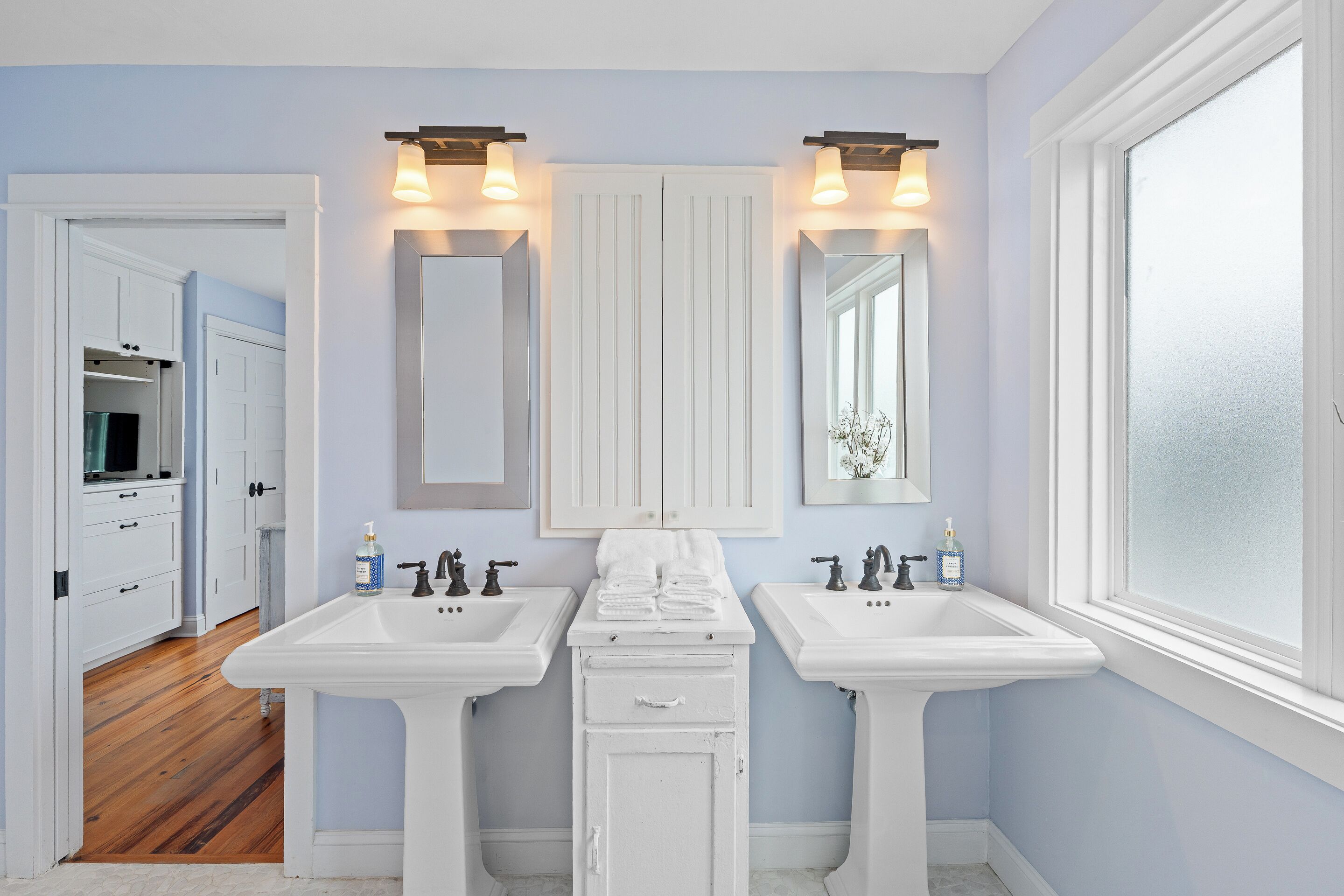 A bathroom with two white sinks, a mirror, and a door leading to a hallway.