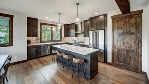 A modern kitchen with a large island, bar stools, wooden flooring, and dark cabinetry. - Hawk Ridge in the Highlands of Breck | Golf Course and Nordic Trails! (Breckenridge)