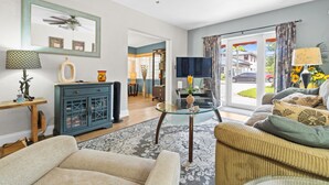 A spacious living room with a large window, a ceiling fan, and a dining area visible through an open door. - Cozy 2BR Snowbird Home Near Wilton Manors (Fort Lauderdale)