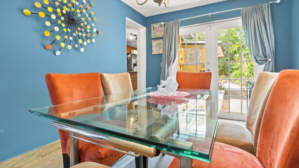 A dining area with a glass table, orange chairs, and a colorful wall decoration. - Cozy 2BR Snowbird Home Near Wilton Manors (Fort Lauderdale)