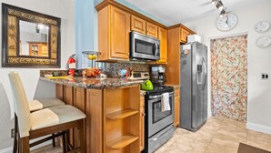 A kitchen with wooden cabinets, a microwave, a stove, and a refrigerator. - Cozy 2BR Snowbird Home Near Wilton Manors (Fort Lauderdale)