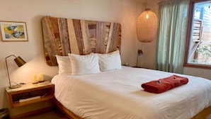 Een netjes opgemaakt bed met witte lakens, een rode handdoek en een houten hoofdbord.