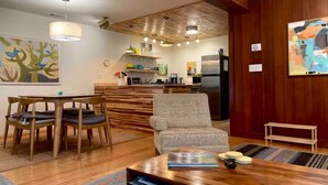 Een moderne woonkamer met een houten eettafel, een gestreept fauteuil en een keuken op de achtergrond.