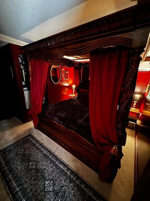 A four-poster bed with red curtains, a round mirror, and a small table with a lamp. - Sunset Cabin-Adults Only Hot Tub Getaway (Hillsboro)