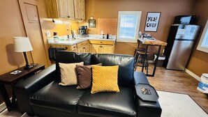 A compact living space with a black leather sofa, wooden cabinets, a kitchenette, and a dining area. - Sunset Cabin-Adults Only Hot Tub Getaway (Hillsboro)