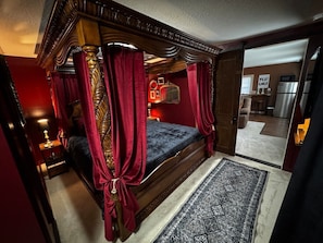 A bedroom with a four-poster bed, a nightstand, a mirror, and a rug.