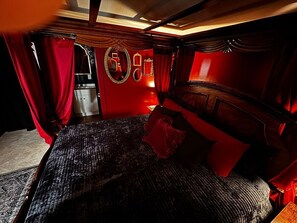 Una habitación con cama, cortinas rojas y un espejo en la pared.