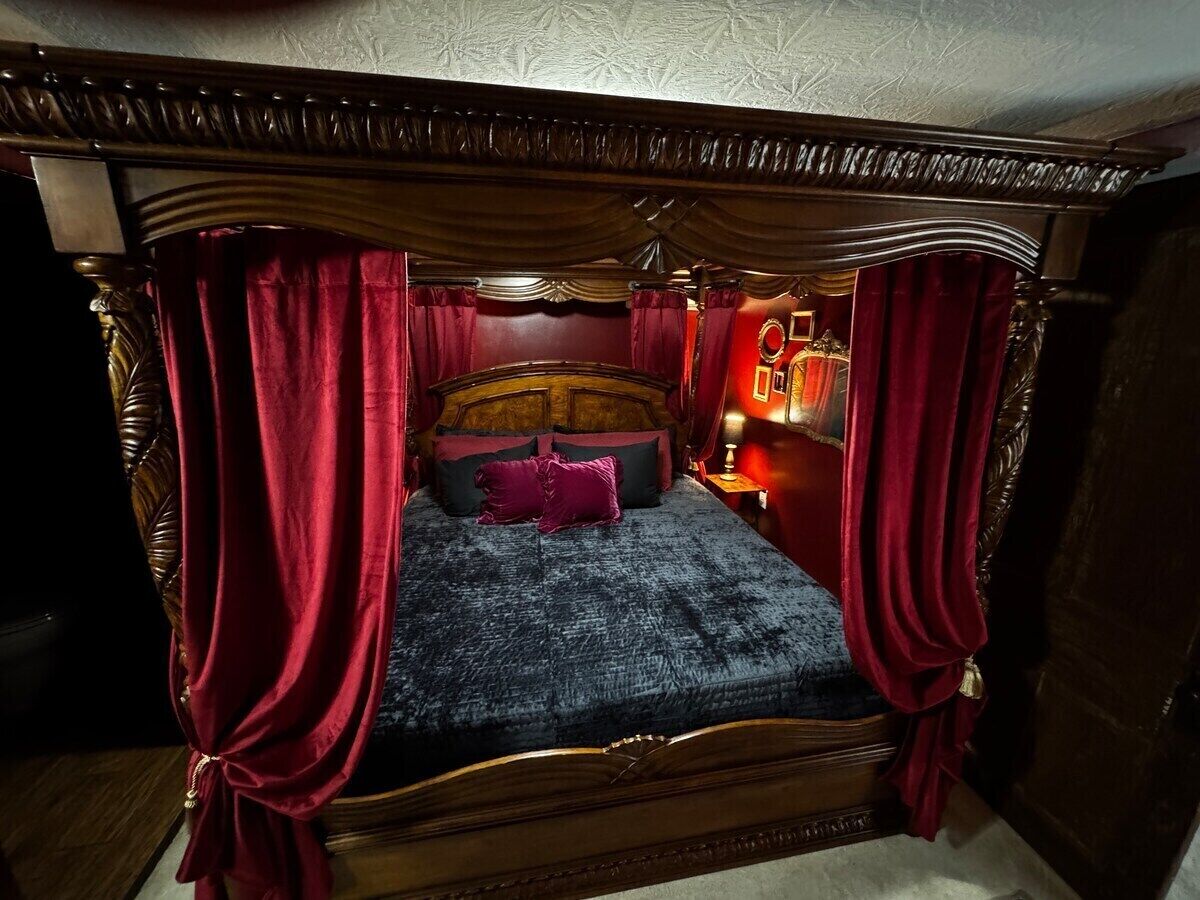 Un lit à baldaquin avec des rideaux rouges, une couvre-lit bleu foncé et de nombreux coussins.