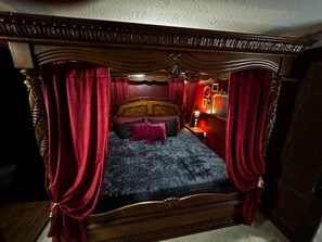 Un lit à baldaquin avec des rideaux rouges, une couvre-lit bleu foncé et de nombreux coussins.