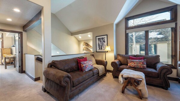 A spacious living room with two leather sofas, a small wooden stool, and a large window providing a view of the outside.
