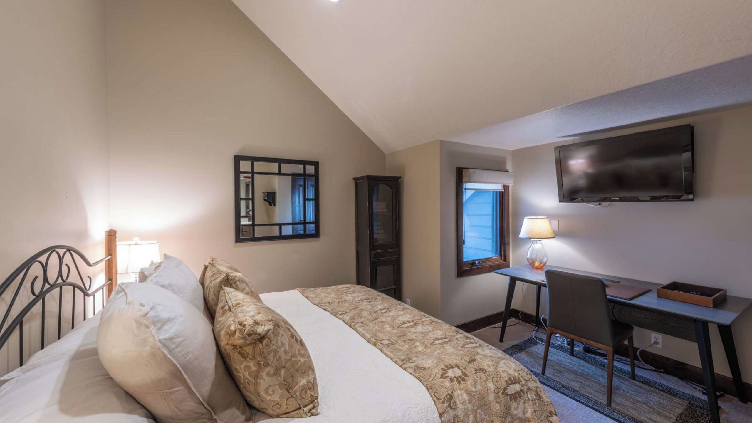 A hotel room with a bed, a desk, a chair, a TV, and a mirror.