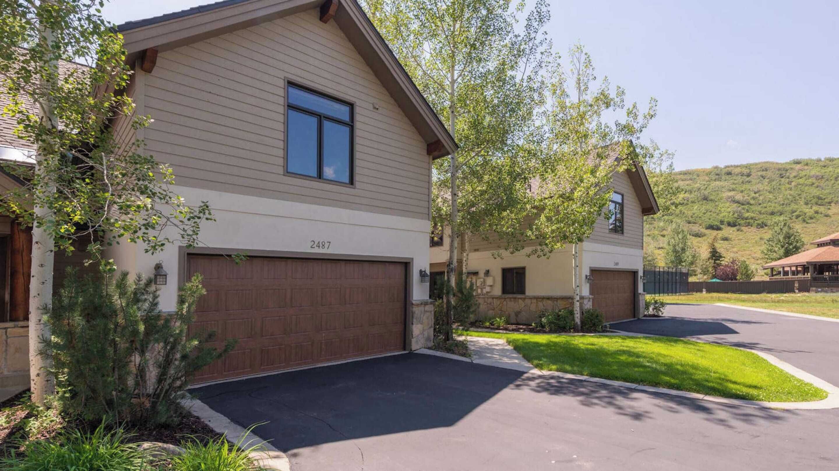 A two-story residential building with a garage, number 2487, surrounded by well-maintained landscaping and a hilly backdrop.