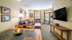 A living room with a dining table, chairs, a sofa, a coffee table, and a TV mounted on the wall.