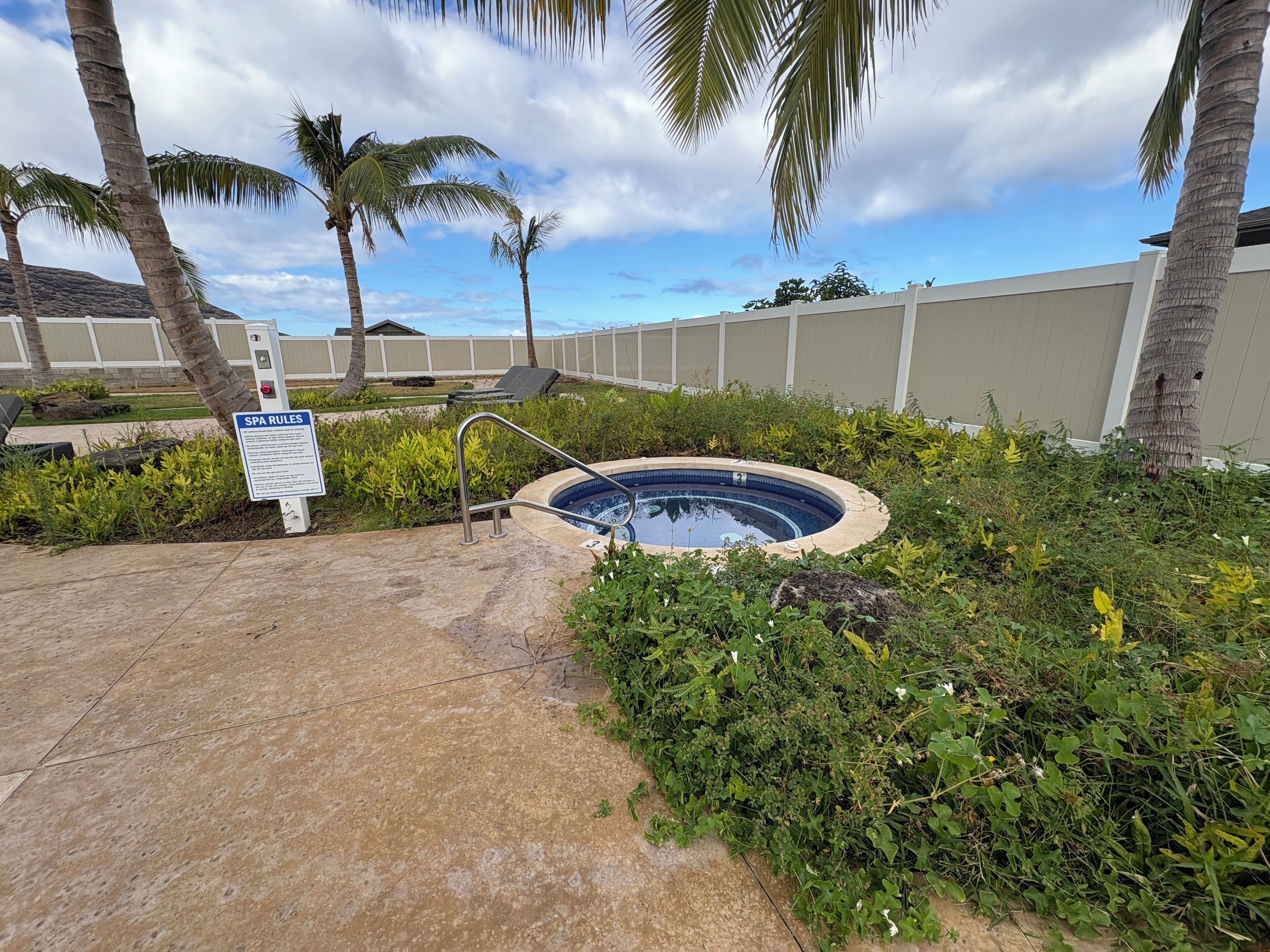 A small outdoor hot tub surrounded by lush greenery and palm trees, with a sign indicating spa rules.