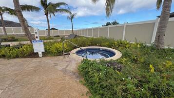 A small outdoor hot tub surrounded by lush greenery and palm trees, with a sign indicating spa rules.