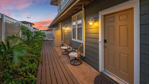 Une maison d’habitation dotée d’une terrasse en bois, de deux chaises et d’une porte avec un luminaire.