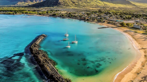Une ville côtière dotée d’eaux turquoise et limpides, d’une plage de sable et d’une digue rocheuse.
