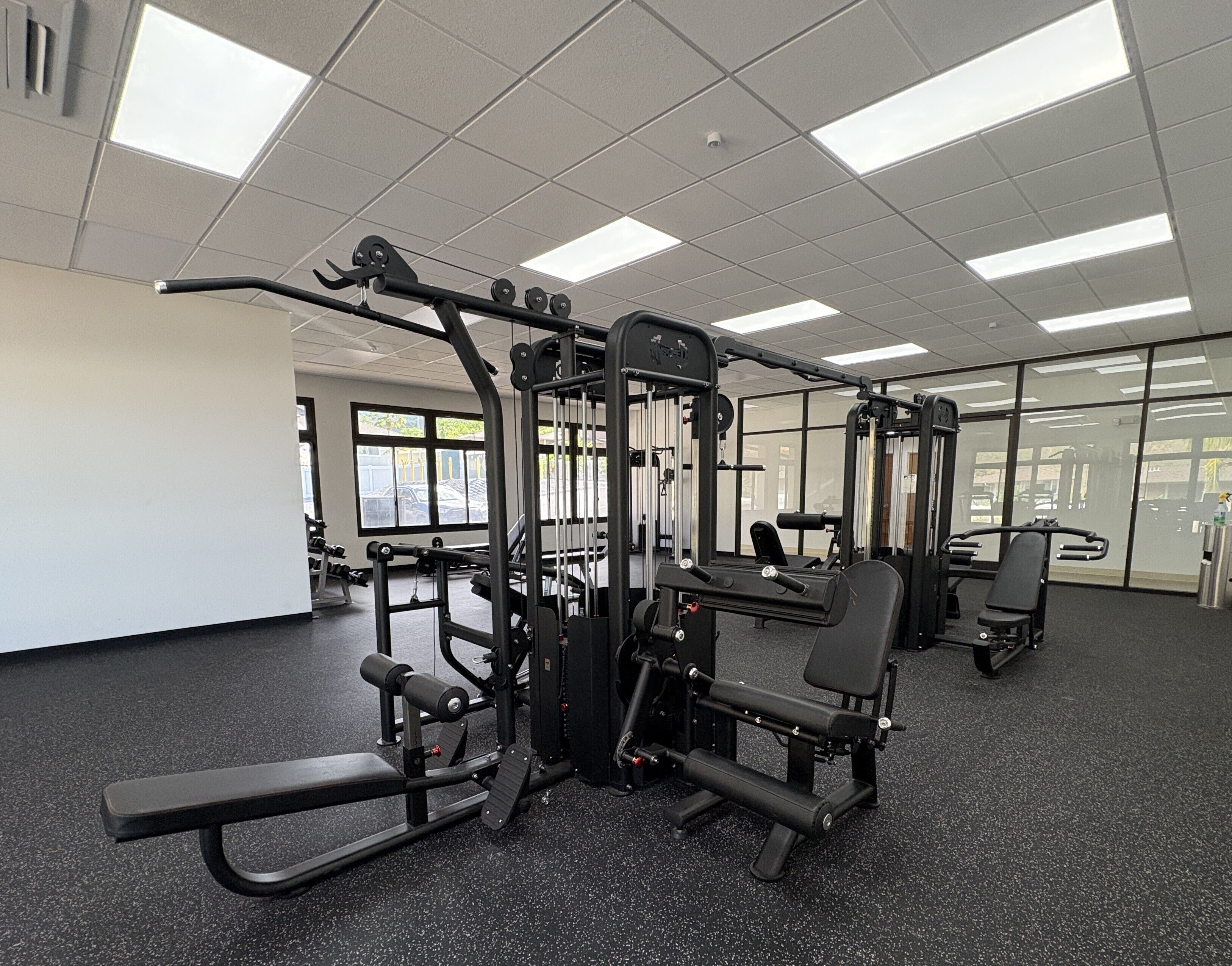 A gym with various exercise machines, large windows, and a tiled ceiling.
