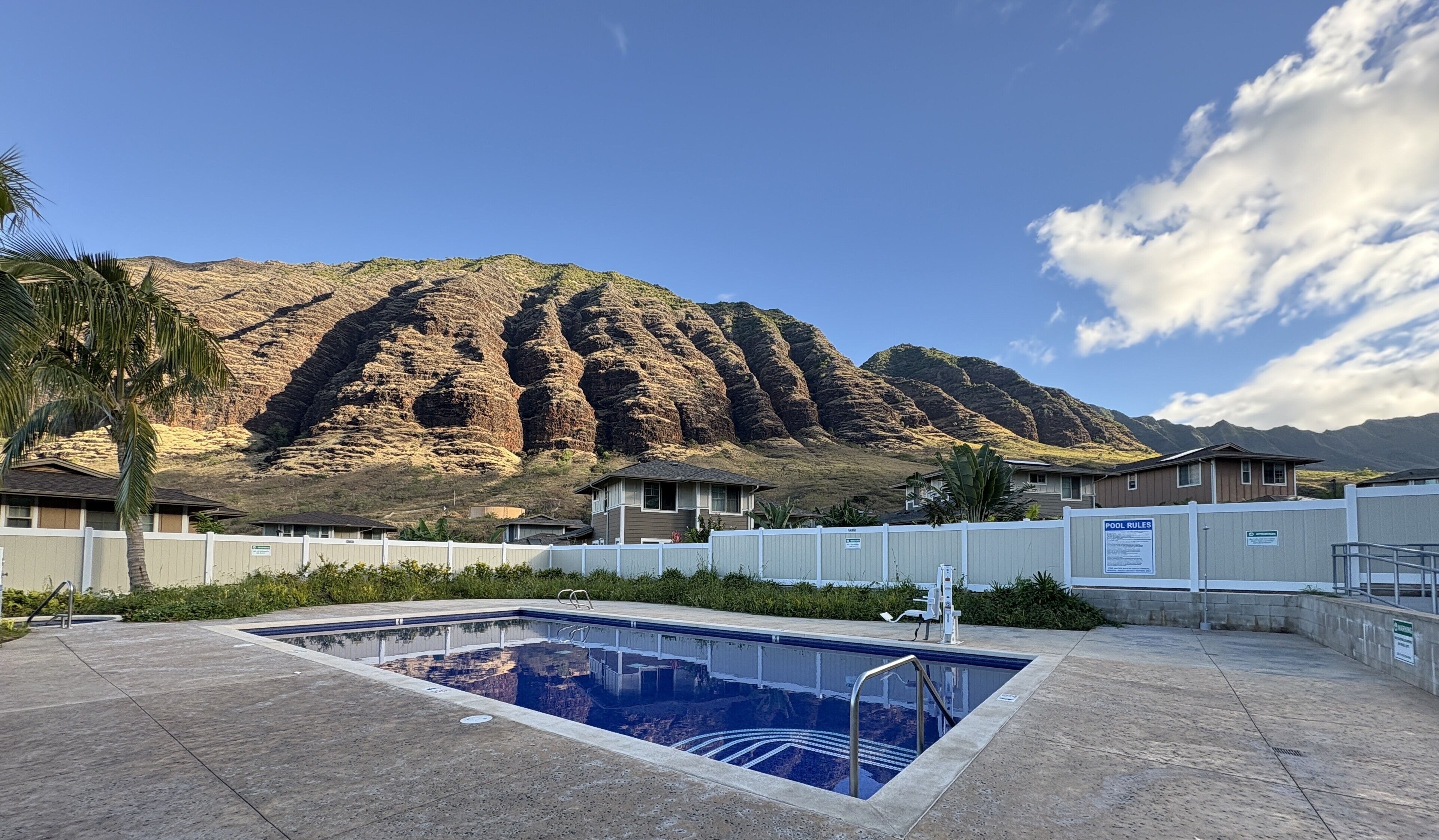 Piscina con montañas al fondo, rodeada de casas y una zona vallada.