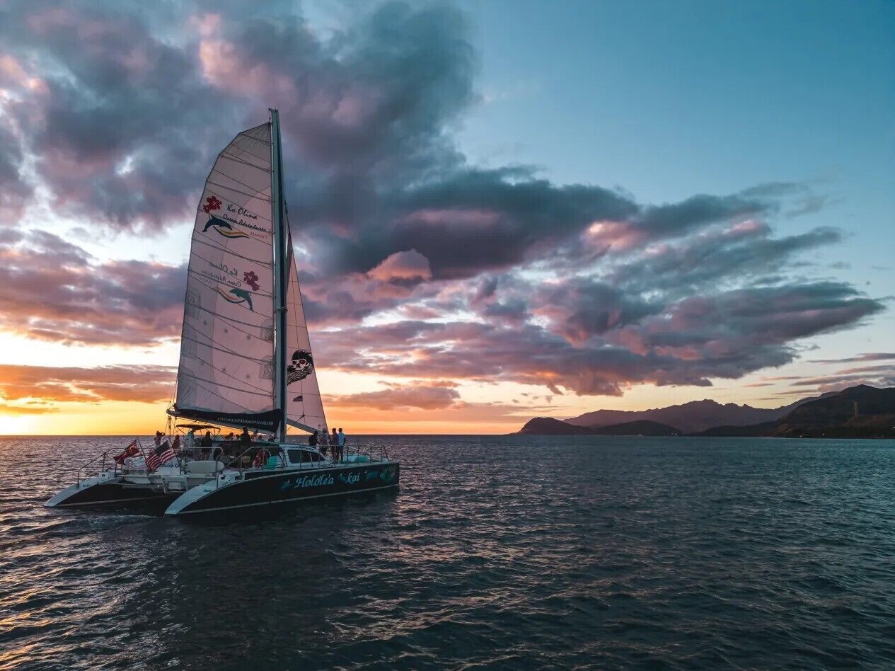 Un voilier doté d’une cabine et de sièges sur le pont, naviguant sur une étendue d’eau au coucher du soleil.