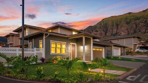 Une maison à deux étages avec un jardin devant, un garage et une vue sur les montagnes en arrière-plan.